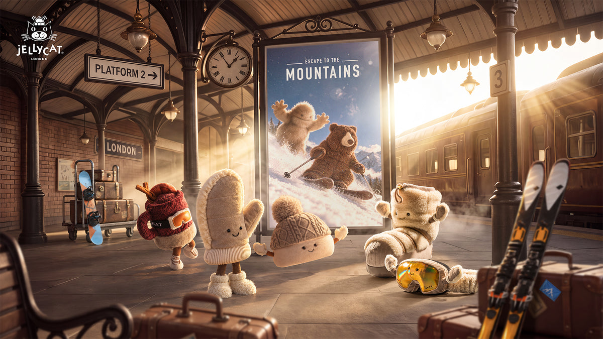 Jellycat plush mitten, beanie, snow boot, ski goggles and cocoa mug on a train station platform